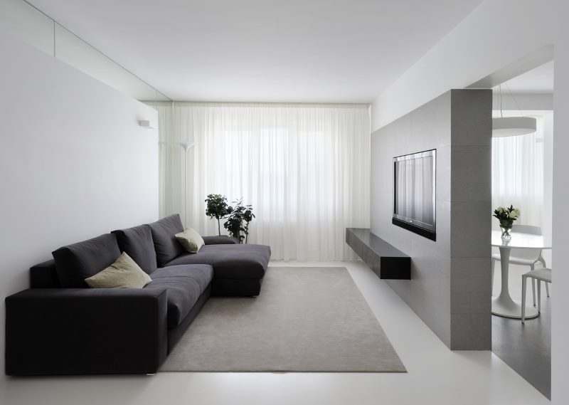 Juoda sofa minimalistinio stiliaus gyvenamajame kambaryje